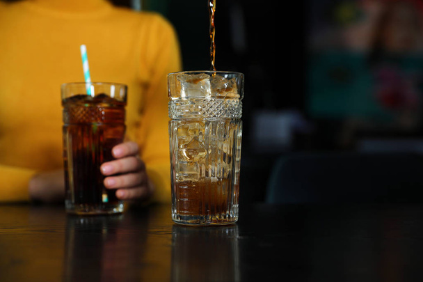 Pouring refreshing cola into glass and blurred woman on background - Fotografie, Obrázek