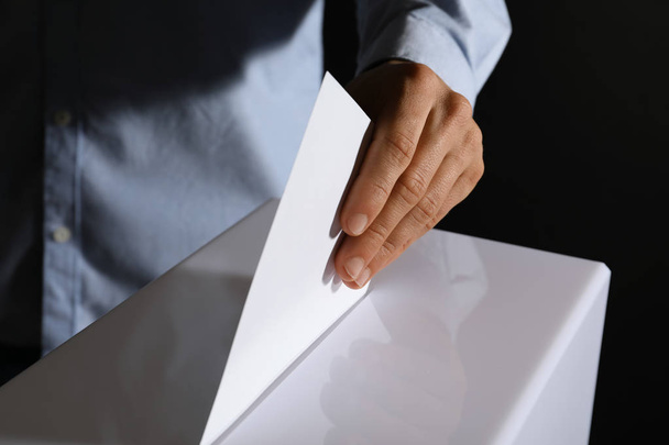 Человек кладет свой голос в урну для голосования на черном фоне, крупным планом
 - Фото, изображение