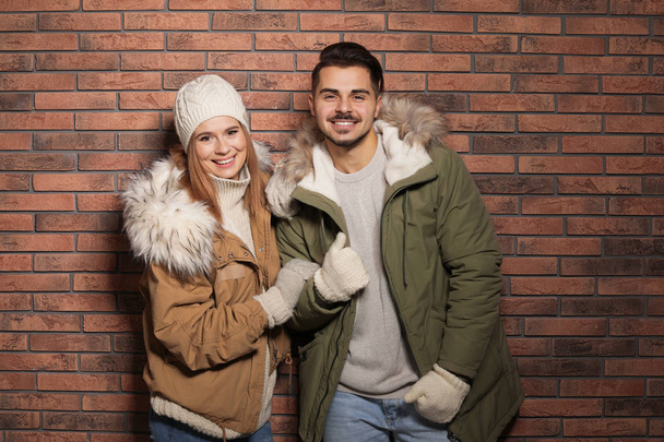 Casal jovem vestindo roupas quentes contra a parede de tijolo. Pronto para férias de inverno
 - Foto, Imagem