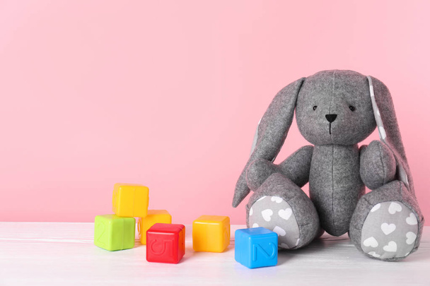 Adorable toy bunny and plastic cubes on table against color background, space for text. Child room elements - Fotoğraf, Görsel