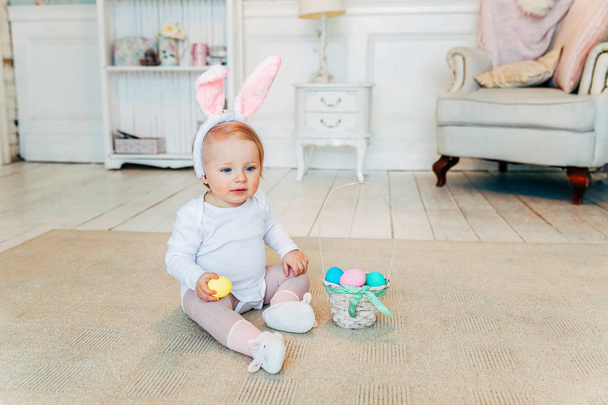 Дитину Дівчинка носіння кролик вуха в день Великодня. Дівчинка тримає кошик з фарбовані яйця, сидячи на підлозі будинку, отримавши задоволення від пасхальне яйце полювання. Щасливого Великдень свято святкування весна концепції - Фото, зображення