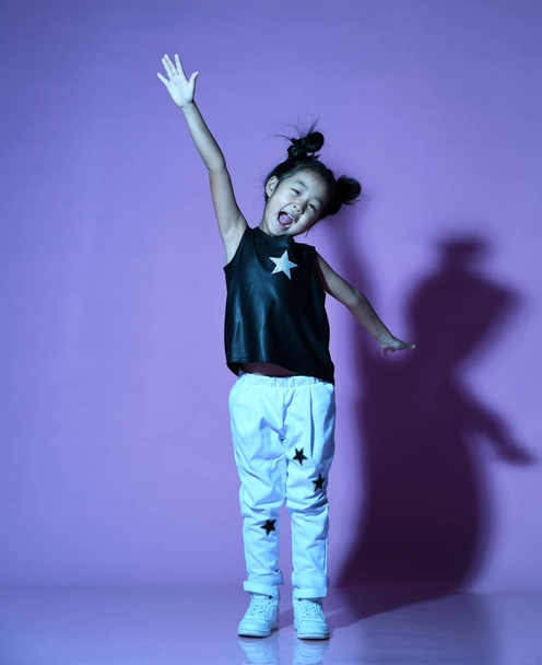 Asian kid girl in shirt and pants with stars stand with a hand up and shouts - Foto, afbeelding