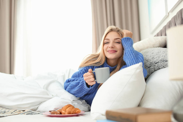 Beautiful young woman lying with breakfast in bed at home. Winter atmosphere - Foto, Bild