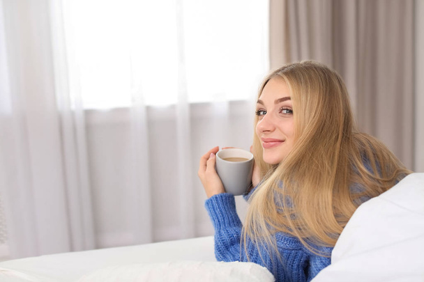 Красива молода жінка лежить з чашкою в ліжку вдома. Зимова атмосфера
 - Фото, зображення