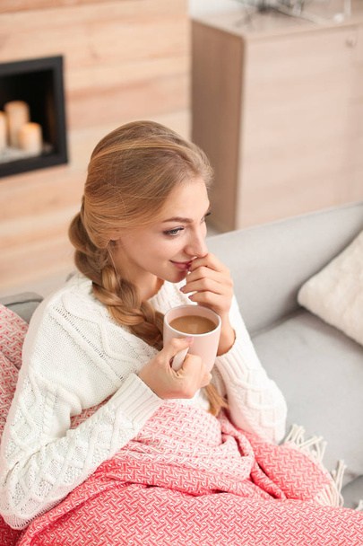 Beautiful young woman sitting on sofa with cup at home. Winter atmosphere - Foto, Imagem