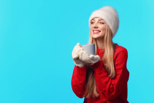 Portrait of emotional young woman in stylish hat, sweater and mittens with cup on color background, space for text. Winter atmosphere - Φωτογραφία, εικόνα