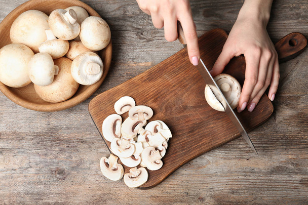 Young woman cutting fresh champignon mushrooms on wooden board, top view - Фото, изображение