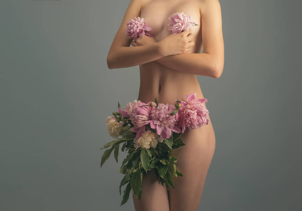 Žena. Koncept prsa a vagíny. Dámské zdraví a krásy. Lázně a lékařství. Růžové pivoňky na nahé ženské tělo. Spodní prádlo pro ženy. Móda a příroda. Ekologický koncept. Velkou výhodou mladé ženy - Fotografie, Obrázek