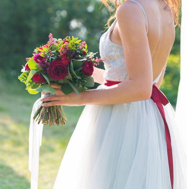 the bride is holding a bright red wedding bouquet of fresh flowers and eucalyptus - Fotoğraf, Görsel