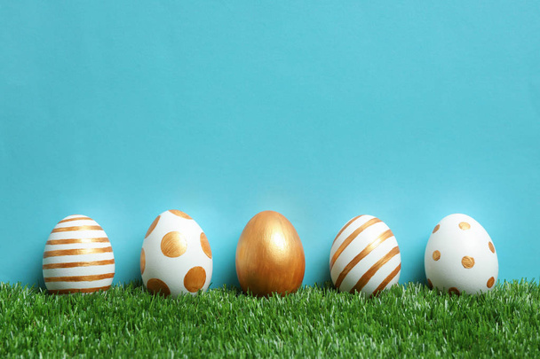 Line of traditional Easter eggs decorated with golden paint on green lawn against color background, space for text - Foto, imagen