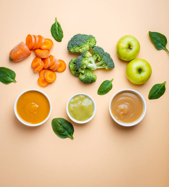 White bowls with healthy natural baby food on pastel background. Purees, made of fresh organic fruit and vegetables, flay lay, top view, concept. Kids food made from carrot, broccoli, apples, spinach - Photo, Image