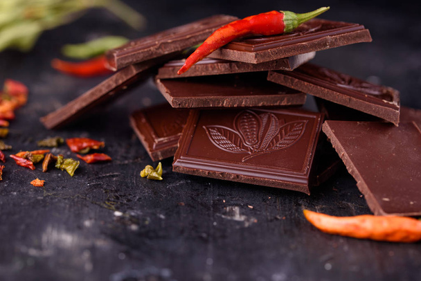 Natural black chocolate with red bitter pepper on a black background. - Photo, Image
