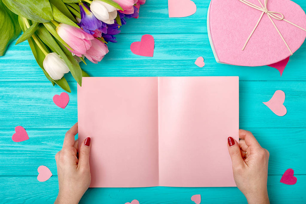Valentines Day background with bouquet of tulips, a card with hearts and a gift.Female hands open a postcard. - Foto, Imagen