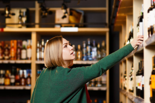 Foto de mujer sobre fondo borroso de estantes con botellas de vino
 - Foto, Imagen