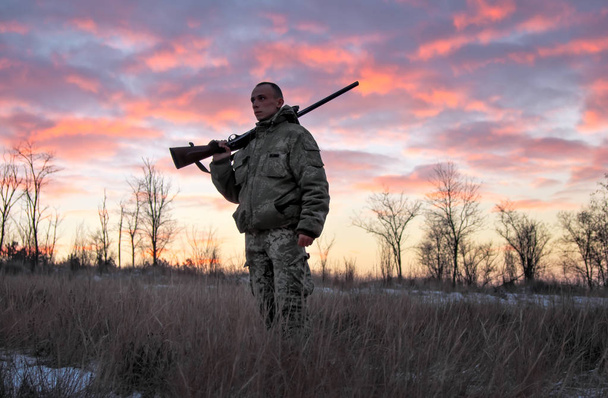Winterjagd bei Sonnenaufgang. Jäger bewegt sich mit Schrotflinte auf Beutesuche. - Foto, Bild