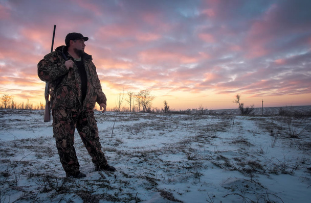 Winterjagd bei Sonnenaufgang. Jäger bewegt sich mit Schrotflinte auf Beutesuche. - Foto, Bild