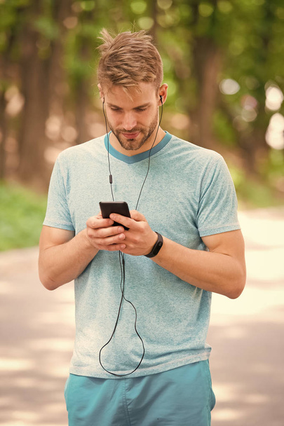 Man athlete on busy face setting up fitness tracker with smartphone app, nature background. Sportsman training with pedometer gadget. Athlete with fitness tracker or pedometer. Sport gadget concept - Photo, image