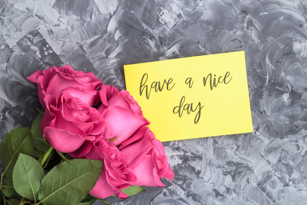 romantisches Konzept. Rote Rosen und Schriftzug wünschen einen schönen Tag auf grauem Betongrund. - Foto, Bild