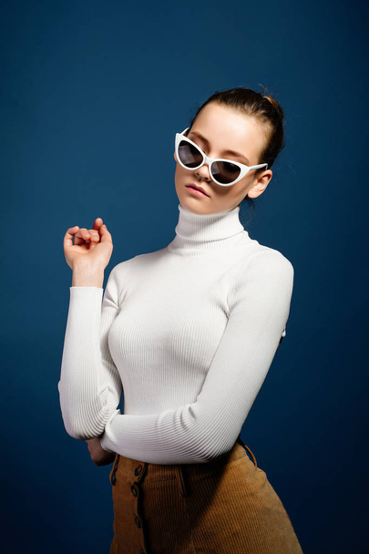 Portrait of a beautiful young girl in sunglasses on a blue background - Foto, Imagem