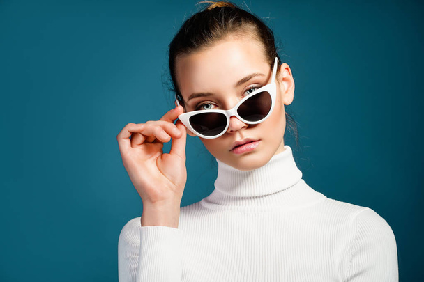 Portrait of a beautiful young girl in sunglasses on a blue background - Foto, Bild