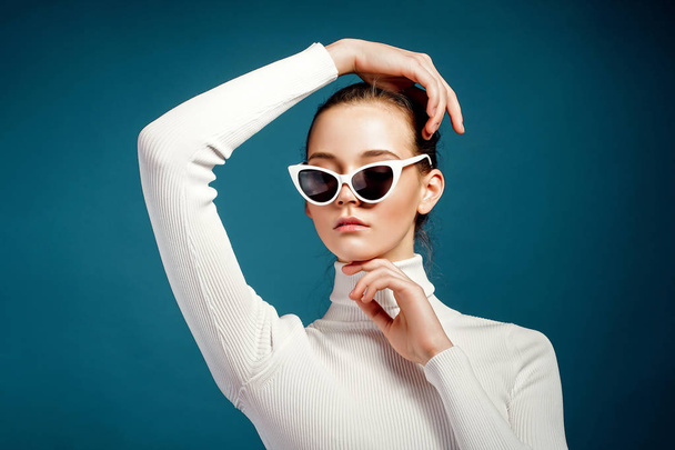 Portrait of a beautiful young girl in sunglasses on a blue background - Fotoğraf, Görsel