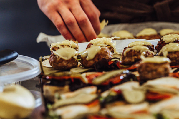 Chef masculino poniendo ingredientes de hamburguesas en un pan rebanado extendido sobre una mesa - Concepto de la persona trabajadora y la higiene en la cocina, aspecto de película vintage
 - Foto, Imagen