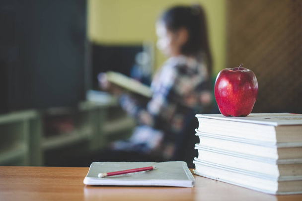school thema afbeelding bestaande uit een appel en een stapel boeken de achtergrond is een student zitten lezen van een boek. - Foto, afbeelding