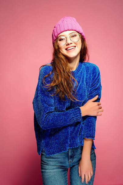 Jovem mulher moderna vestindo suéter azul e chapéu rosa posando, fazendo expressão facial engraçada
. - Foto, Imagem