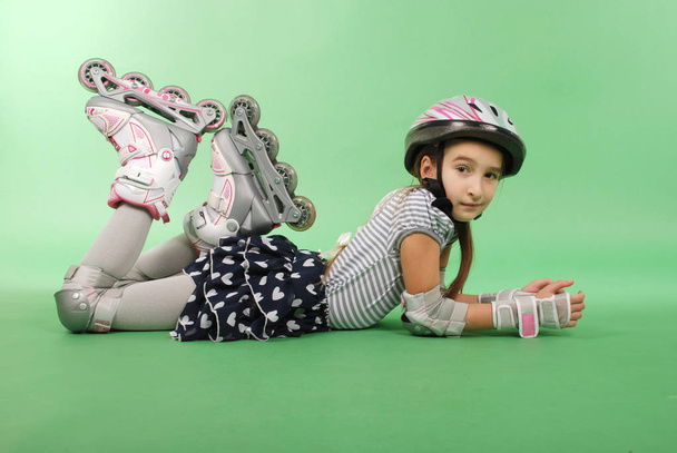 Pretty girl with rollerskates lying on green background - Photo, Image
