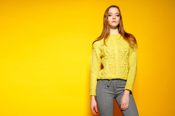 Beautiful female model wears casual comfrotable sweater, poses against yellow background. Copyspace - Photo, image