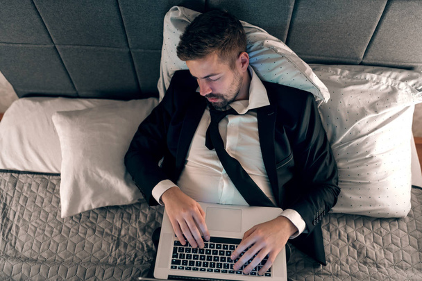Молодий бізнесмен спить у ліжку з ноутбуком. Руки на клавіатурі. Концепція перевантаження
. - Фото, зображення