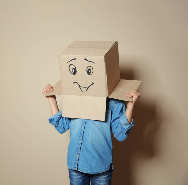 Cute little child wearing cardboard box with smiling face on color background - Foto, afbeelding