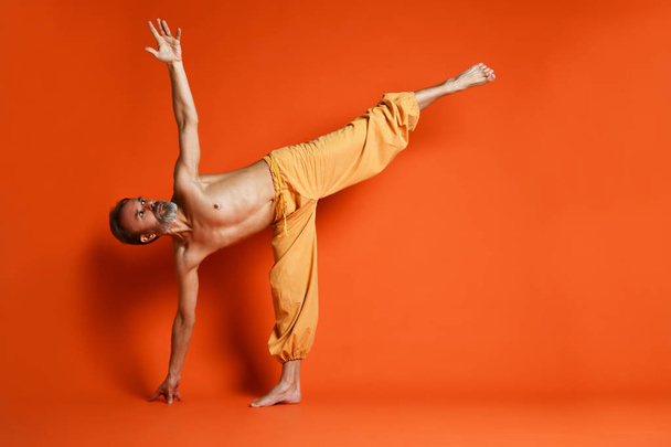Vieil homme pratiquant le yoga faire des exercices d'étirement sur fond orange
 - Photo, image