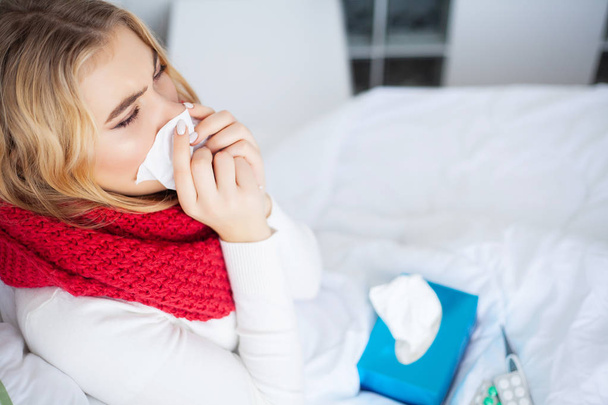 Sairas nainen. Nainen, jolla on flunssavirus makaa sängyssä, hän mittaa lämpötilaansa lämpömittarilla
 - Valokuva, kuva