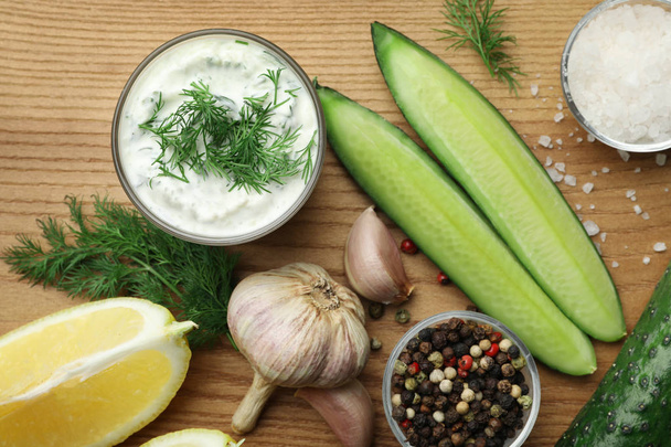 Tzatziki cucumber sauce with ingredients on wooden background, flat lay - 写真・画像