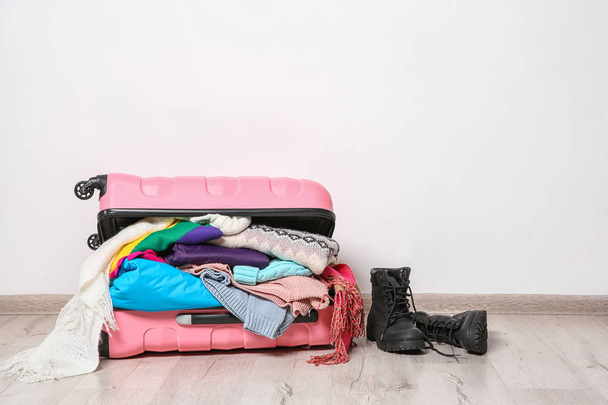 Suitcase with clothes and boots on floor against white wall, space for text. Winter vacation - Foto, immagini