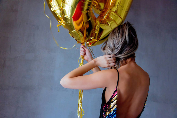 Молодая женщина с золотыми шариками на свой тридцатилетний день рождения. В помещении. Человек в винтажном 80-м платье и прическа. На сером фоне
 - Фото, изображение