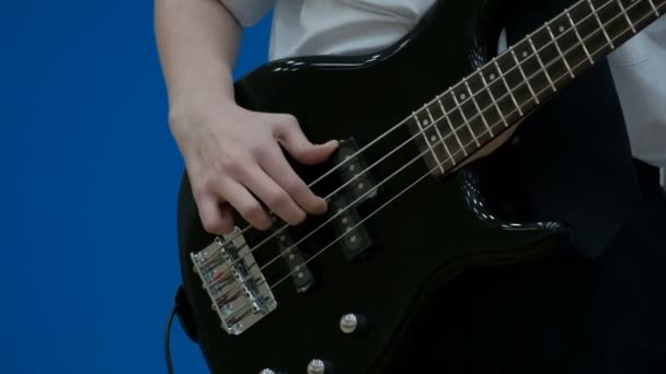 Guy teen baixo guitarrista tocando uma guitarra elétrica preta. Close-up. Os dedos de um adolescente estão puxando cordas em uma guitarra baixo. Conceito tema musical da juventude
. - Filmagem, Vídeo