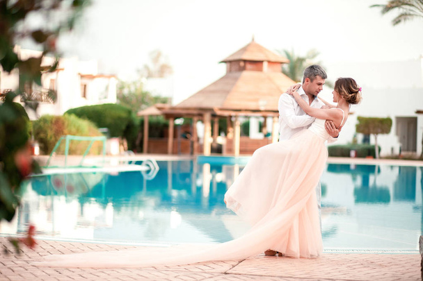 Newly married couple after wedding in luxury resort. Romantic bride and groom relaxing near swimming pool. Honeymoon. Tropical country. - Photo, Image