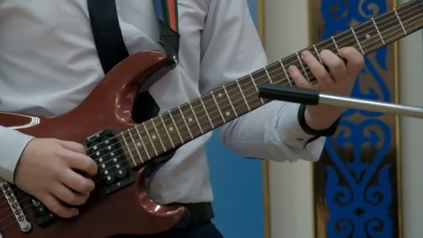 Man duwt tekenreeksen met een pick en frets van de klemmen van de vingers op een solo gitaar. Een tiener in een wit overhemd speelt een bruin elektrische gitaar. Concertuitvoering. Concept op het onderwerp van de muzikale jeugd. - Video