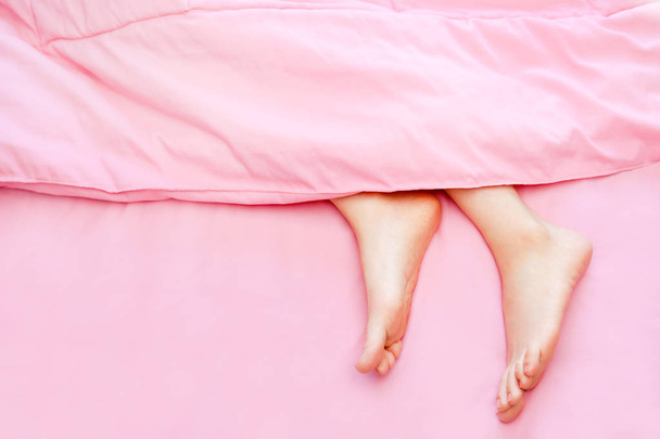 Beautiful Asian Young Woman Body Legs and Feet Isolated on The Pastel Pink Bedroom Background. Female Foot in Bed Sleep Relax. Cropped Image of People Barefoot in Pink Bed Under Blanket at Home. - Foto, imagen