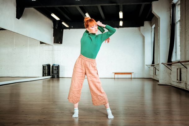 Red haired girl in a green turtleneck doing yoga a gym - Фото, изображение