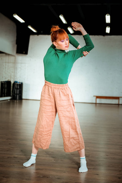 Pretty red haired girl in a green turtleneck doing asana for stretching - Foto, afbeelding