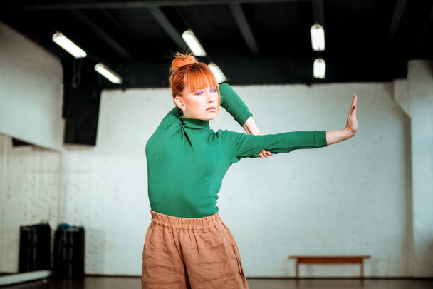 Pretty red haired girl in a green turtleneck standing in asana - Foto, imagen
