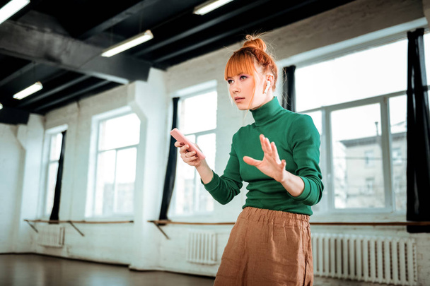 Red-haired professional yoga instructor in a green turtleneck holding a phone in her hand - Fotó, kép