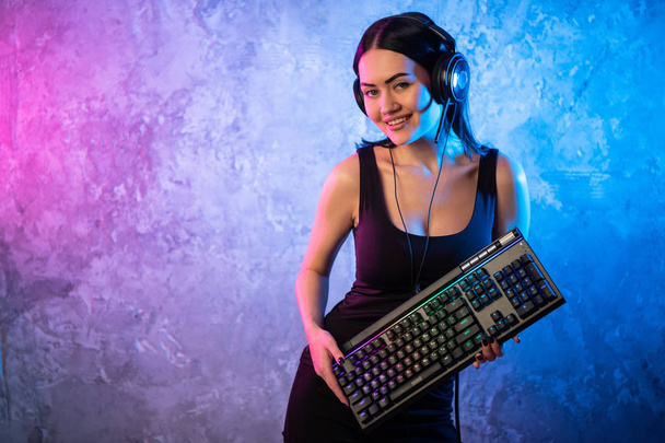Chica profesional Gamer en MMORPG Estrategia Videojuego. Ella posando sobre un colorido fondo azul y rosa con un teclado de juego. Ella usa auriculares para juegos. - Foto, imagen