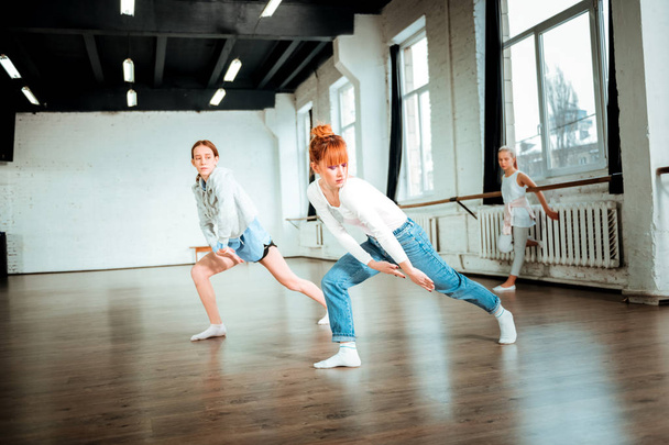 Επαγγελματική μπαλέτο δάσκαλος στο μπλε τζιν και μαθητή της κάνει ρυθμικές κινήσεις - Φωτογραφία, εικόνα