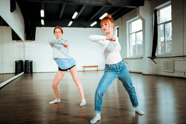 Beautiful red-haired professional dancer in blue jeans and her student moving energetically - Foto, Bild