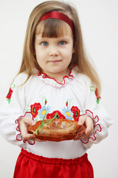 Piccola bella ragazza in costume ucraino in possesso di un piatto con salsiccia
 - Foto, immagini