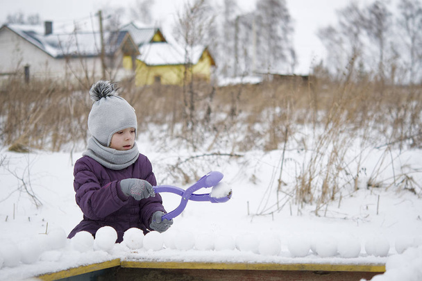 Happy child in warm clothing playing with snow. Child playing with snowball maker.  - Photo, Image